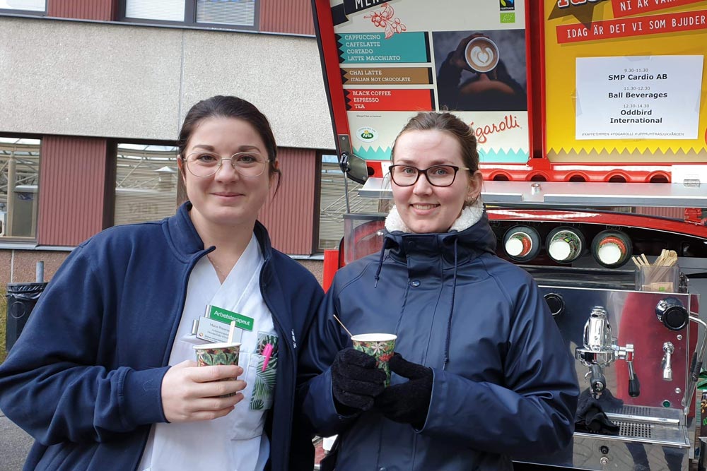 Sjukvårdspersonal som håller i en varsin kaffe och ler mot kameran